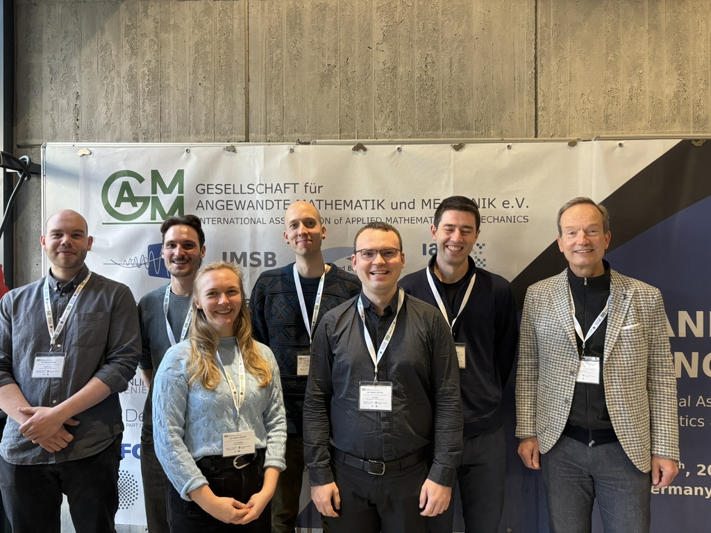 Gruppe von neun Personen mit Namensschildern vor Banner der GM-AGM-Konferenz, Neutral-Porträt.