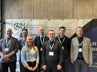 Gruppe von neun Personen mit Namensschildern vor Banner der GM-AGM-Konferenz, Neutral-Porträt.